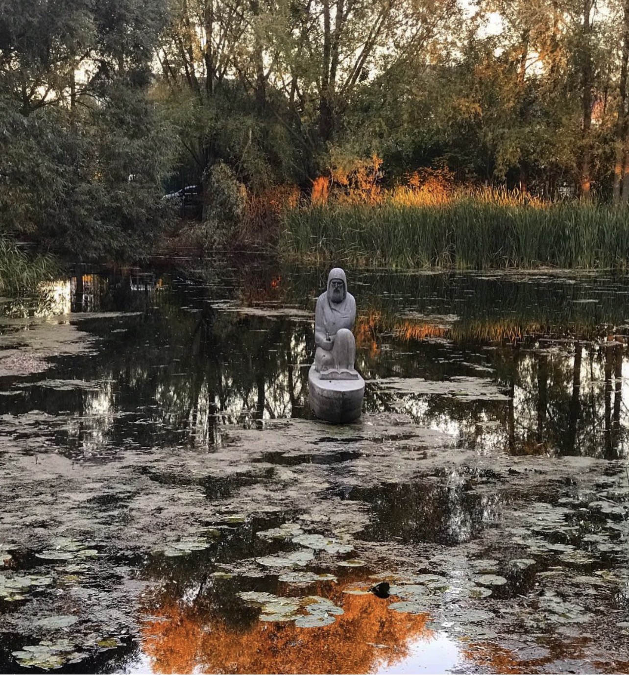 A silent stone guardian standing amid the dark water in the autumn garden of Radomysl Castle